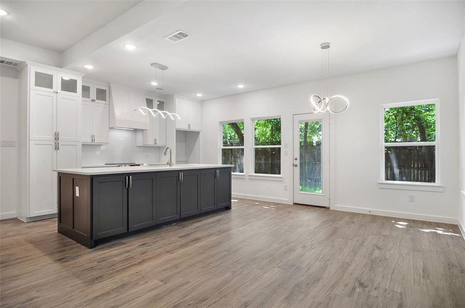 Kitchen with white cabinetry, light wood-type flooring, premium range hood, and a healthy amount of sunlight