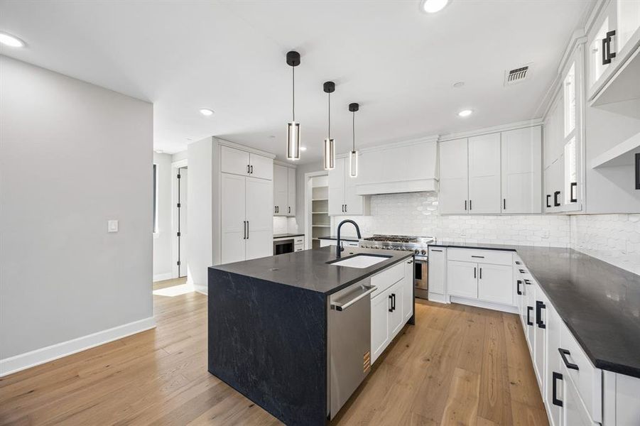 Kitchen with an island with sink, stainless steel appliances, white cabinetry, and light wood finished floors Kitchen with an island with sink, stainless steel appliances, white cabinetry, and light wood finished floors