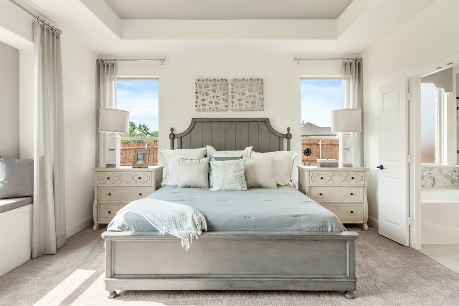 Master bedroom with tray ceiling, gray bed frame, two windows, and matching nightstands on neutral carpet Master bedroom with tray ceiling, gray bed frame, two windows, and matching nightstands on neutral carpet