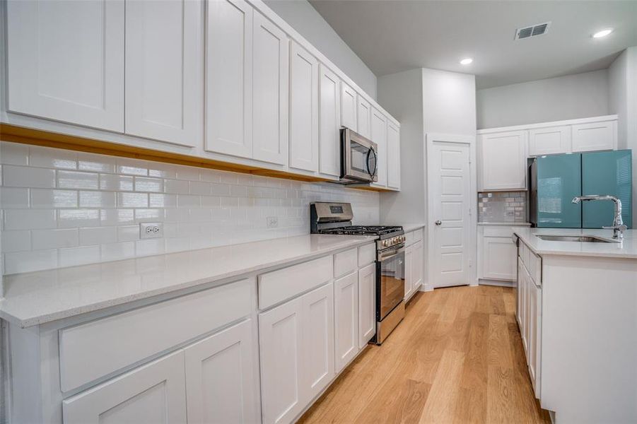 Kitchen featuring stainless steel appliances, white cabinetry, light wood-style floors, decorative backsplash, and light stone counters