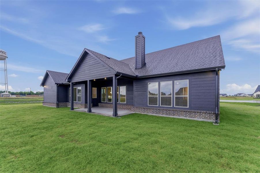 Rear exterior featuring dark siding, a covered patio, multiple windows, a prominent chimney, and a foundational brick skirt Rear exterior featuring dark siding, a covered patio, multiple windows, a prominent chimney, and a foundational brick skirt