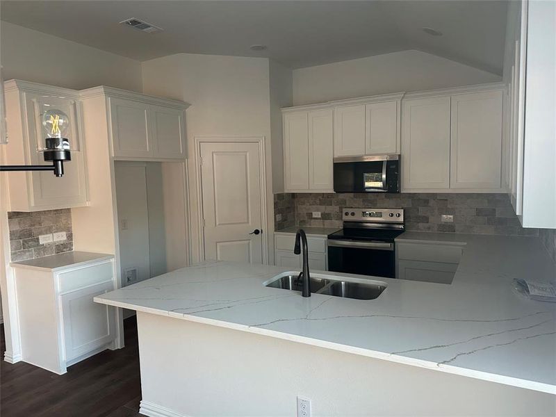 Kitchen with white cabinets, a peninsula, stainless steel appliances, tasteful backsplash, and lofted ceiling