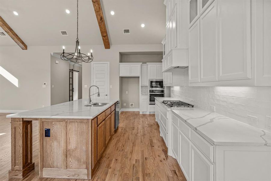 Kitchen featuring white cabinetry, sink, light stone countertops, a barn door, and a spacious island