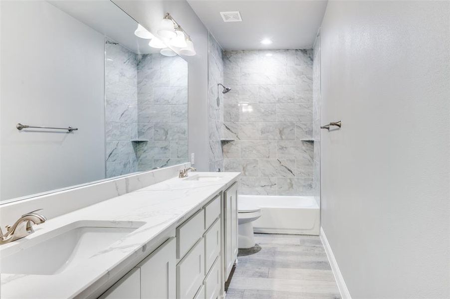 Full bathroom featuring hardwood / wood-style flooring, tiled shower / bath, vanity, and toilet