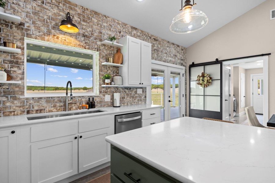 Kitchen with two tone cabinetry, light stone countertops, open shelves, hanging light fixtures, and healthy amount of natural light