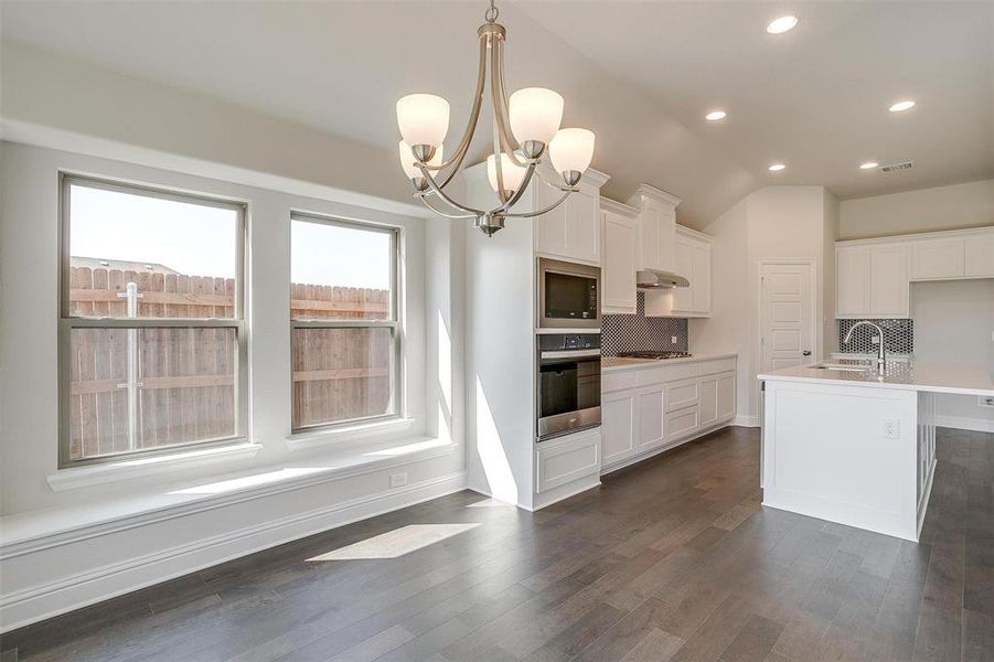 Kitchen with appliances with stainless steel finishes, decorative backsplash, vaulted ceiling, pendant lighting, and a center island with sink