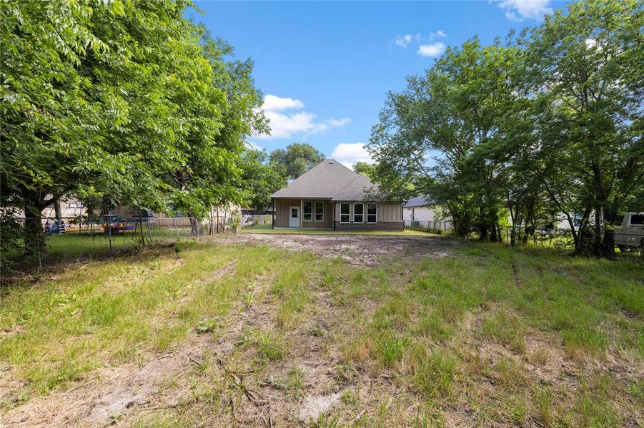 Expansive rear yard with natural grass and mature trees providing perimeter foliage
