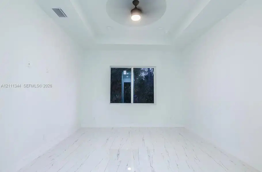 Tray ceiling featuring a central matte black ceiling fan, stone-patterned tile flooring, and a single-pane window Tray ceiling featuring a central matte black ceiling fan, stone-patterned tile flooring, and a single-pane window