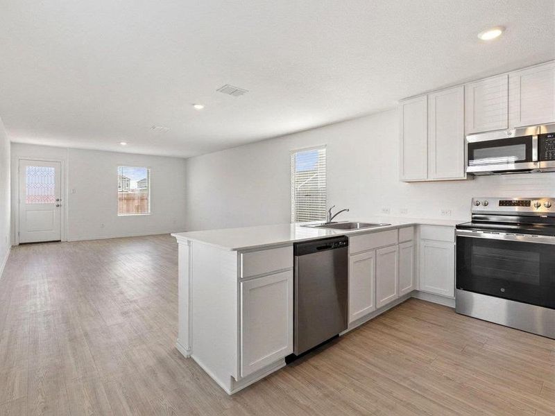 Photo has been enhanced with virtual modification.  Kitchen with stainless steel appliances, a peninsula, recessed lighting, white cabinets, and open floor plan