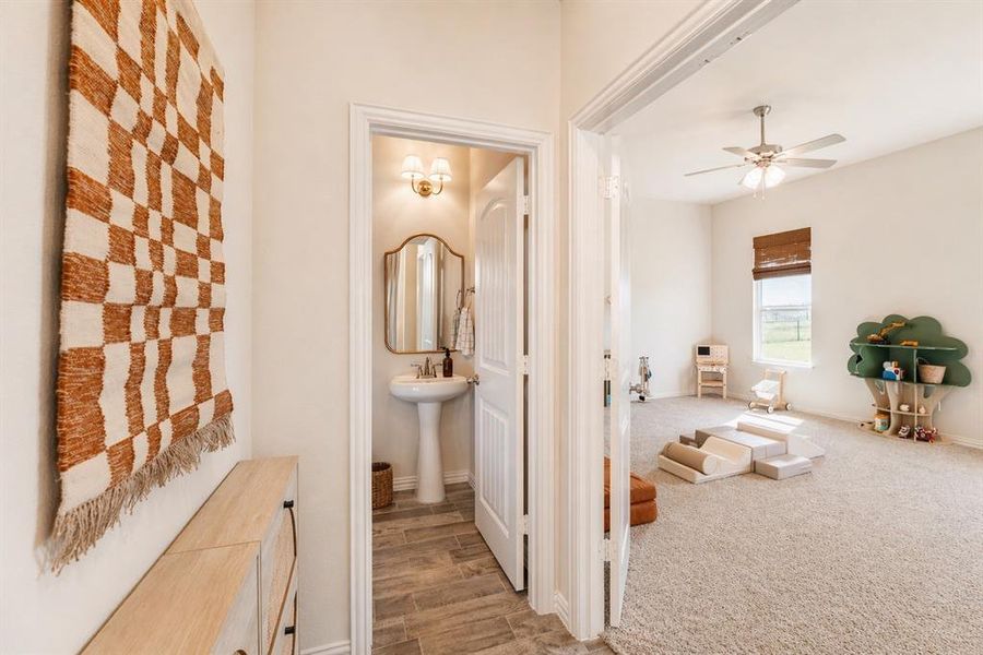 Conveniently located powder room featuring a pedestal sink, framed mirror, and warm-toned wall sconce, with wood-finish flooring