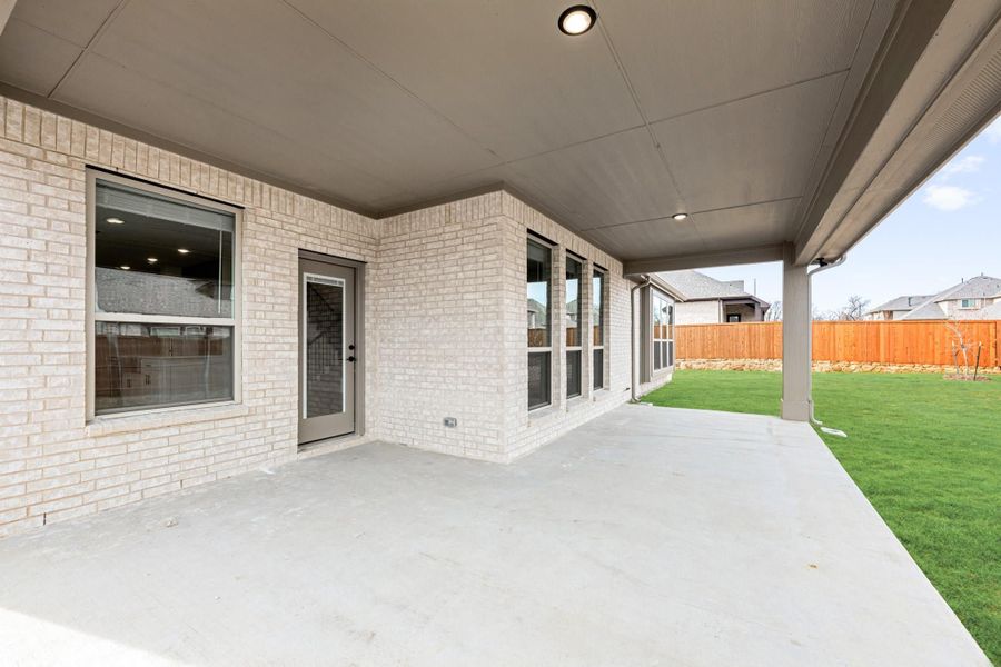 Covered back patio with concrete floor, brick exterior, and fenced green backyard