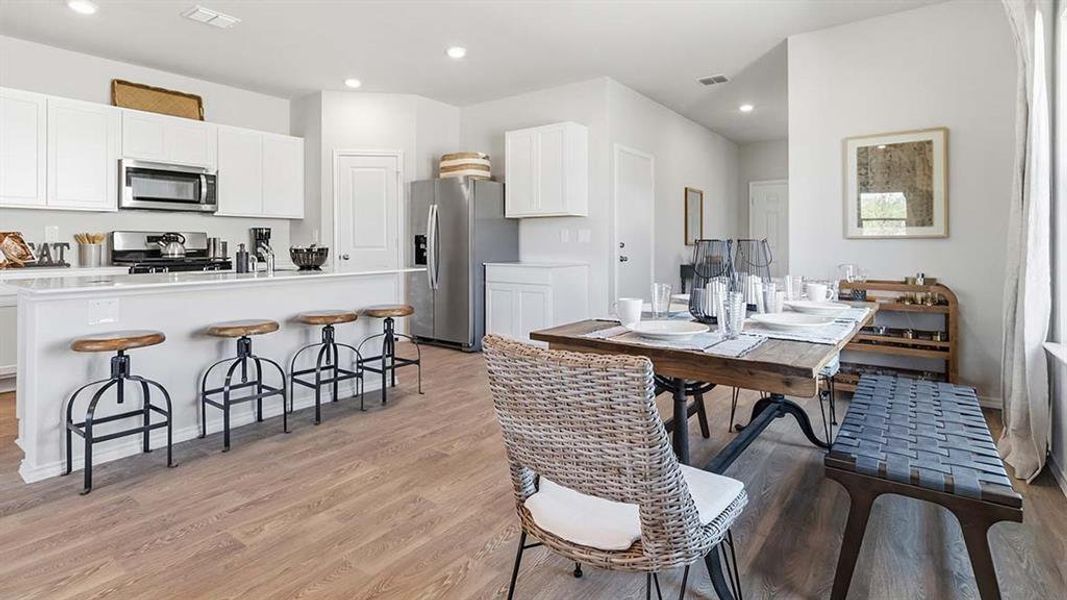 Open-concept kitchen and dining area featuring light wood-finish flooring, white cabinetry, a kitchen island with seating, stainless steel appliances, and abundant natural light
