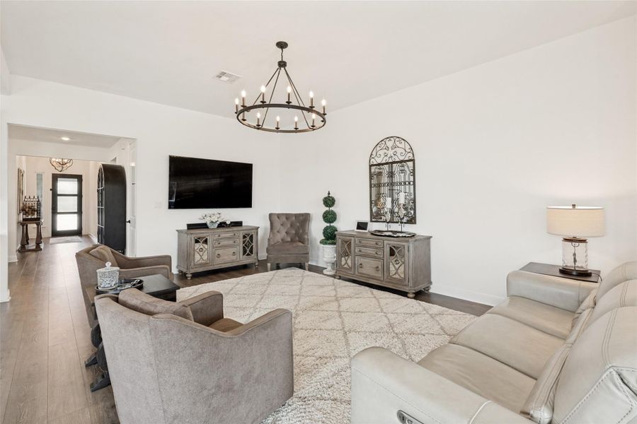 Hardwood floors and a central chandelier ground this airy living room with smooth white walls.