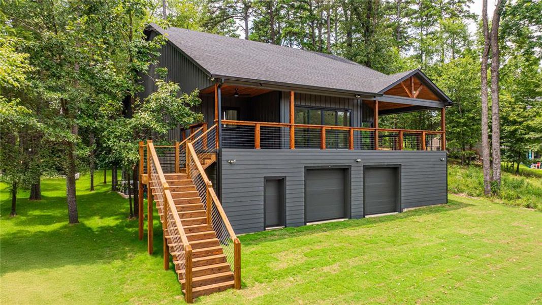 Rear view of property featuring stairway, a yard, a shingled roof, and a garage Rear view of property featuring stairway, a yard, a shingled roof, and a garage