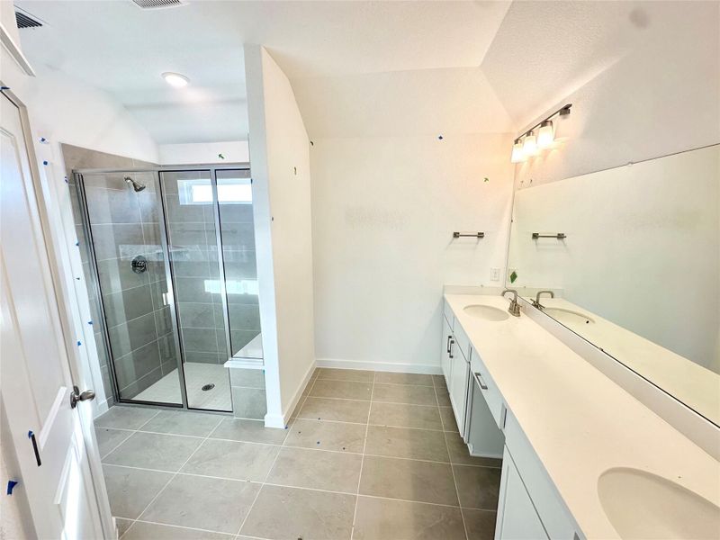 Bathroom with double vanity, a shower stall, and light tile patterned flooring