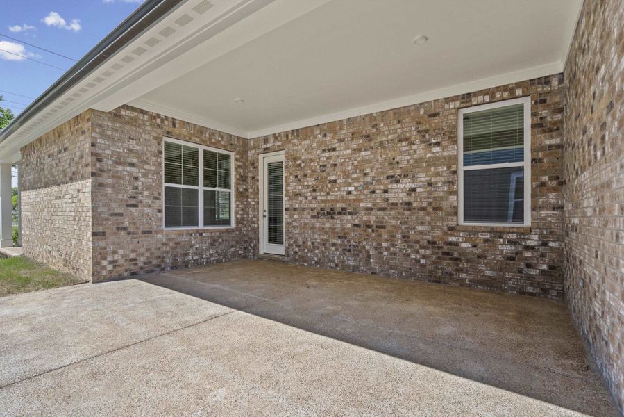 Covered patio featuring a concrete slab, brick exterior, white framed windows, and a glass-paneled door
