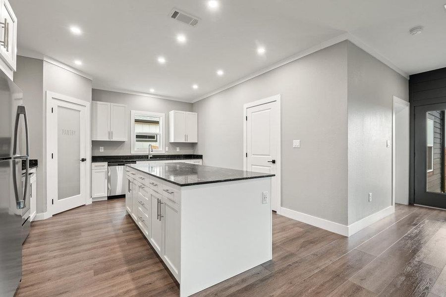 Kitchen with white cabinets, crown molding, a center island, stainless steel appliances, and light wood finished floors