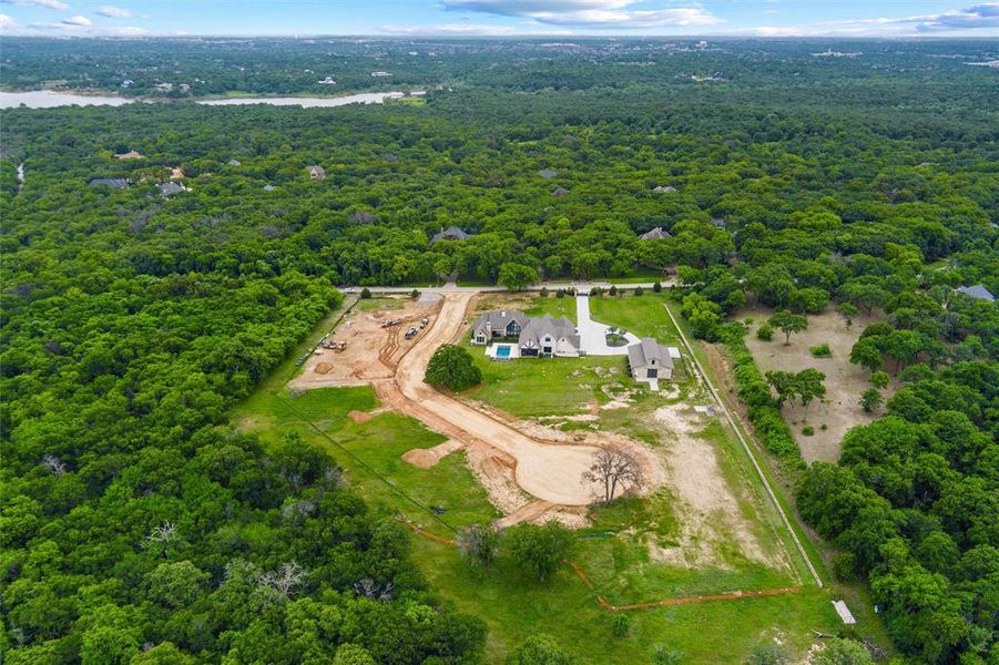 Aerial perspective showcasing extensive tree coverage, a developed residential property with a swimming pool, and multiple building sites in various stages of development Aerial perspective showcasing extensive tree coverage, a developed residential property with a swimming pool, and multiple building sites in various stages of development