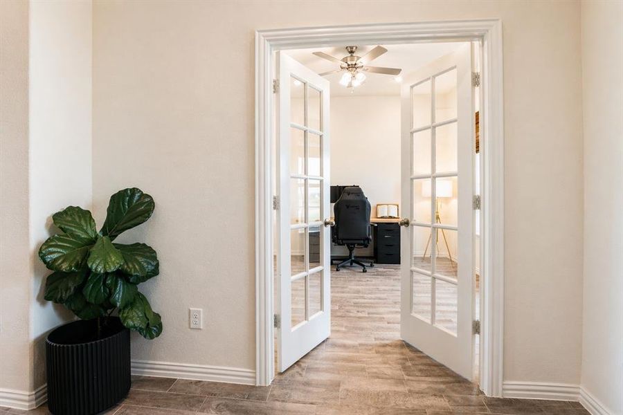 French doors with clear glass panes open into a room featuring wood-finish flooring, a ceiling fan with light fixture, and neutral-toned walls