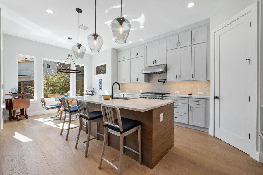 Kitchen with backsplash, an island with sink, a breakfast bar, light stone countertops, and hanging light fixtures
