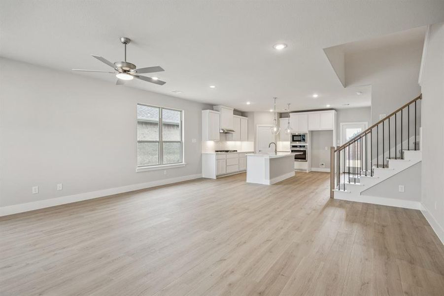 Unfurnished living room featuring stairs, light wood-type flooring, a ceiling fan, and recessed lighting Unfurnished living room featuring stairs, light wood-type flooring, a ceiling fan, and recessed lighting