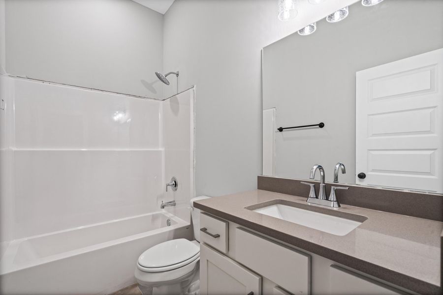 Bathroom featuring a white integrated tub and shower unit, a vanity with a light countertop, an undermount sink, a silver-toned faucet, and a large mirror Bathroom featuring a white integrated tub and shower unit, a vanity with a light countertop, an undermount sink, a silver-toned faucet, and a large mirror
