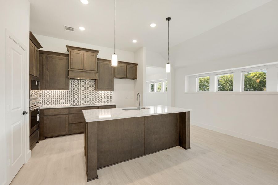 Kitchen with dark wood cabinets, large island, patterned tile backsplash, and pendant lights over light hardwood floors