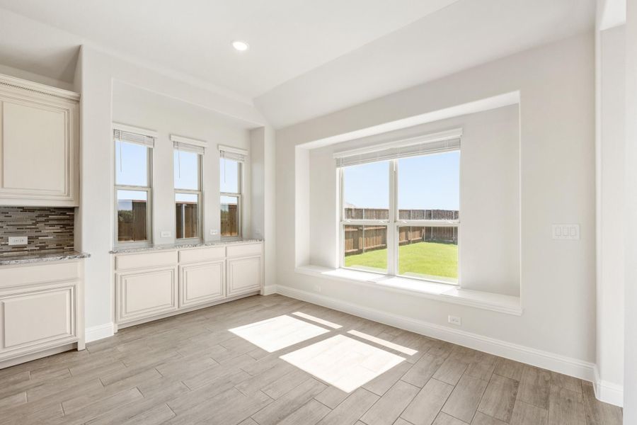 Bright dining area with large window seat, wood-look tile floors, and white cabinetry with granite counters nearby. Bright dining area with large window seat, wood-look tile floors, and white cabinetry with granite counters nearby.