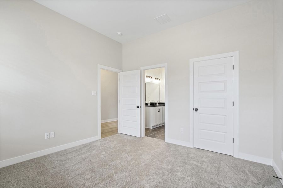 Carpeted room featuring light gray walls, white trim, and a white five-panel door with black hardware Carpeted room featuring light gray walls, white trim, and a white five-panel door with black hardware