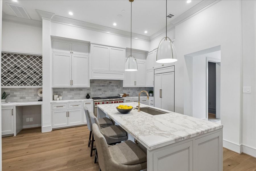One side of the kitchen island features both storage and a counter for casual dining. Norman pendants light the island. At the back right is the walk-in pantry, and at the left is the custom-paneled Sub-Zero refrigerator freezer. The Wolf range features 2 ovens, six burners, and an infrared griddle.