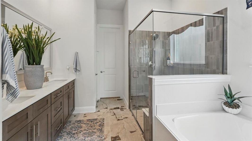 Bathroom featuring a double vanity with stone countertops, a frameless glass shower enclosure with tile surround, a built-in bathtub, and mosaic tile flooring