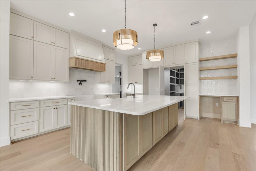 Kitchen with decorative backsplash, a large island, light wood-type flooring, light stone countertops, and two tone cabinetry
