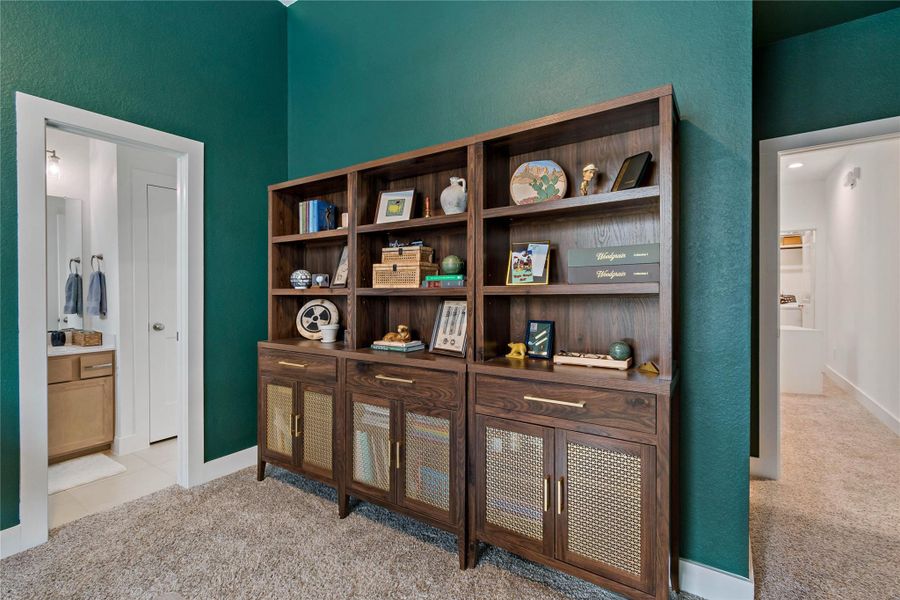Elegant living space featuring a rich green accent wall and a stylish wooden bookshelf with ample storage, seamlessly connecting to a cozy carpeted area and a modern en-suite bathroom. Elegant living space featuring a rich green accent wall and a stylish wooden bookshelf with ample storage, seamlessly connecting to a cozy carpeted area and a modern en-suite bathroom.