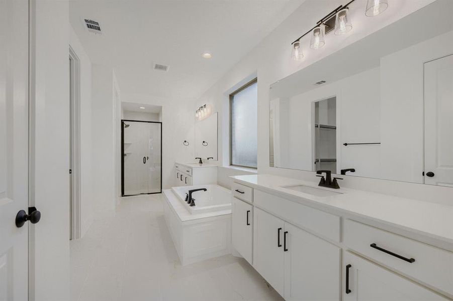 White bathroom featuring a glass-enclosed shower, a built-in soaking tub with black fixtures, and a dual vanity with white cabinetry and countertops