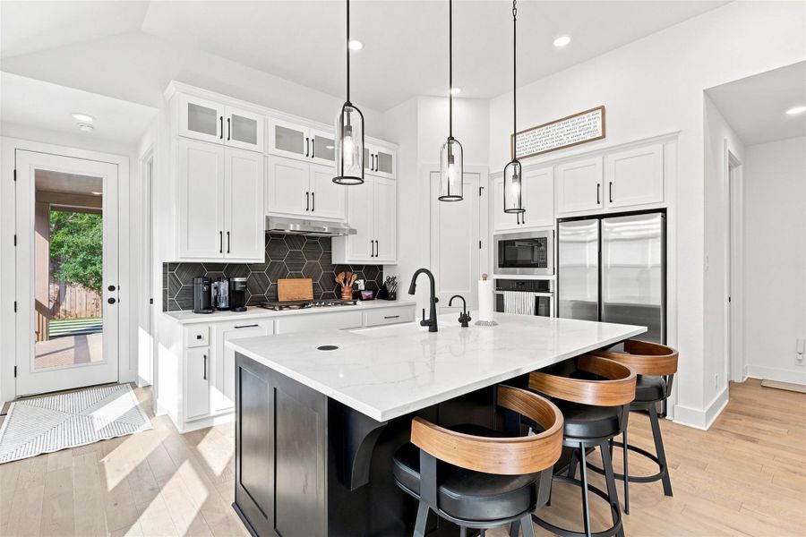Sleek stone countertops and pristine cabinetry frame this modern culinary space with hardwood flooring.