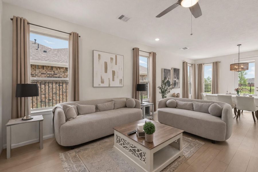 Sunlit open-concept living and dining with wide-plank wood floors, ceiling fan, and oversized windows.