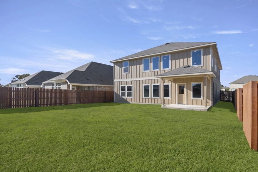 Image of the back exterior of a two story home with green grass, a wooden fence, and a blue sky Image of the back exterior of a two story home with green grass, a wooden fence, and a blue sky