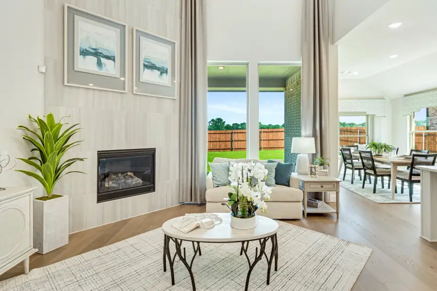 Open living room with two-story fireplace, large windows, and adjacent dining area with hardwood floors