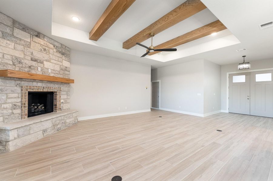 Unfurnished living room with beam ceiling, a stone fireplace, wood tiled floors, and ceiling fan Unfurnished living room with beam ceiling, a stone fireplace, wood tiled floors, and ceiling fan