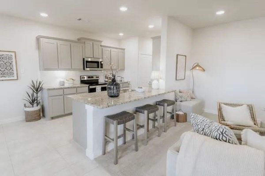 Kitchen with a kitchen bar, open floor plan, light stone countertops, gray cabinetry, and appliances with stainless steel finishes Kitchen with a kitchen bar, open floor plan, light stone countertops, gray cabinetry, and appliances with stainless steel finishes