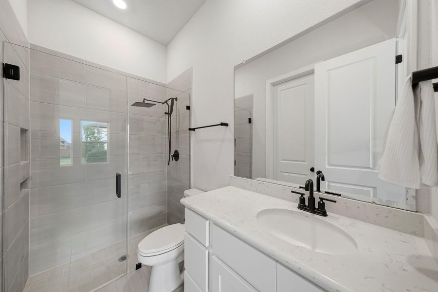 The secondary bath is appointed with 12" x 24" tile flooring, a Quartz-topped vanity, recessed lighting, and a walk-in closet providing generous additional storage. A frameless glass shower elevates the space with a rain shower head, separate spray wand, full tile surround, and built-in shampoo niche, creating a beautifully finished bath with a distinctly upscale feel.