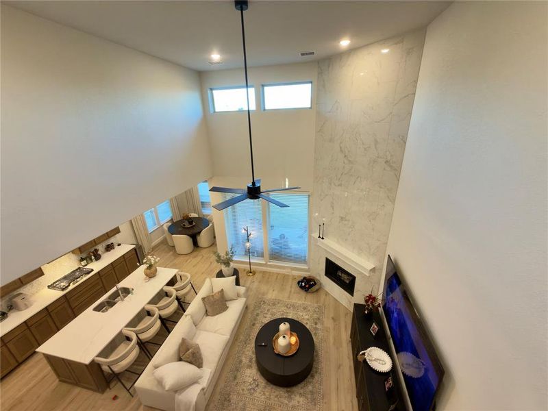 Living area featuring light wood-style floors, a fireplace, a high ceiling, ceiling fan, and plenty of natural light