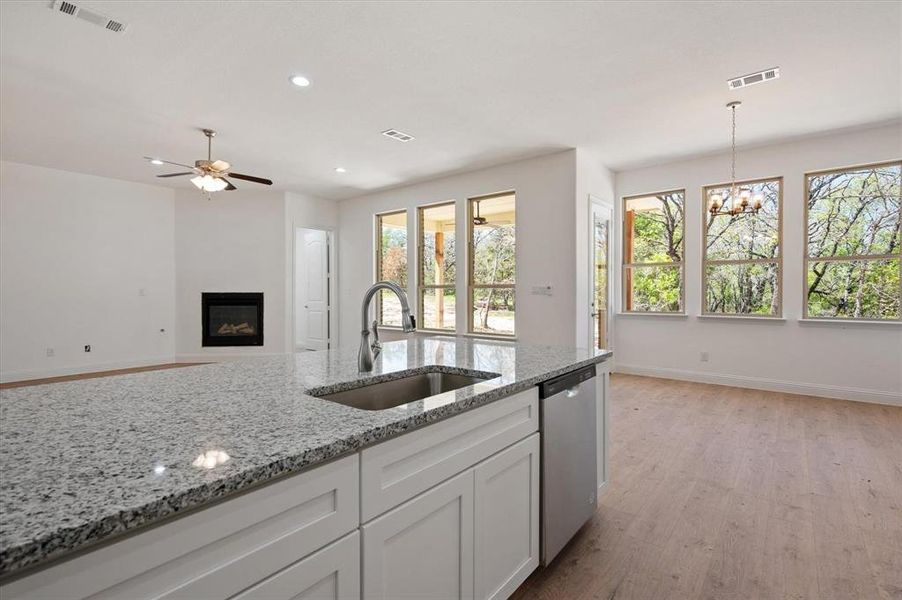 Kitchen with white cabinets, light stone countertops, dishwasher, light hardwood / wood-style floors, and sink