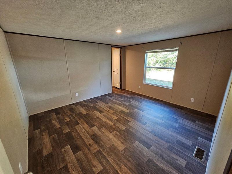 Unfurnished bedroom featuring dark wood-style flooring, a textured ceiling, and a closet Unfurnished bedroom featuring dark wood-style flooring, a textured ceiling, and a closet