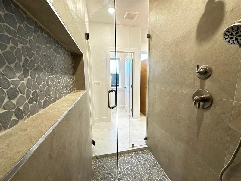 Bathroom with marble finish floor, a tile shower, and visible vents