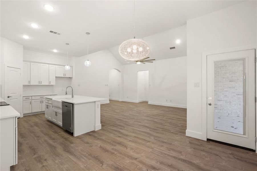 Kitchen with dark wood-type flooring, sink, pendant lighting, a center island with sink, and white cabinets