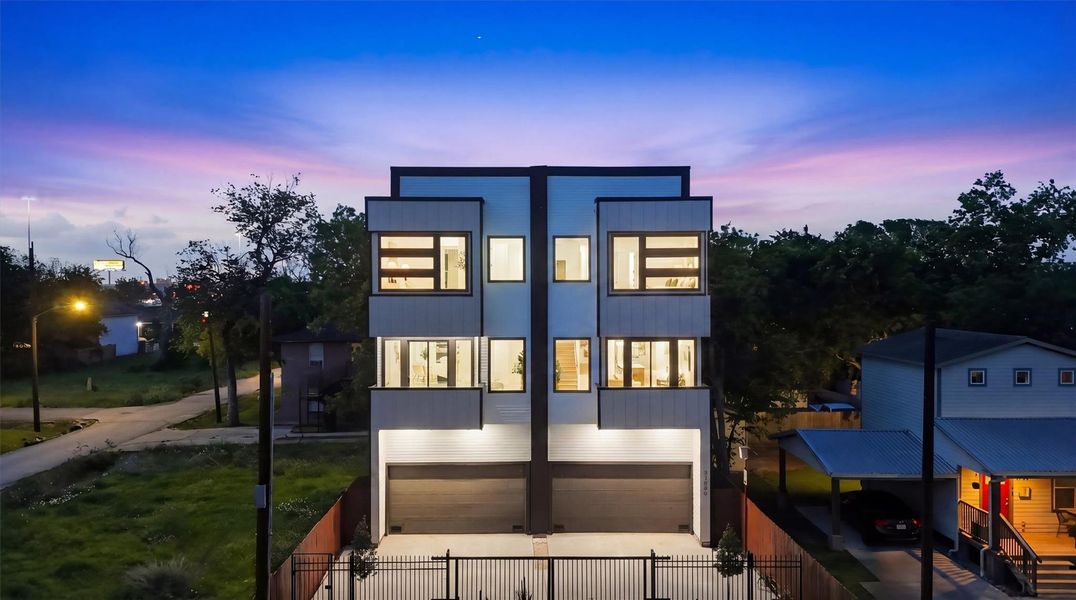 Striking three-story modern duplex illuminated at twilight, featuring sleek contemporary architecture, oversized windows, private garages, and gated entry for exceptional curb appeal and urban sophistication.