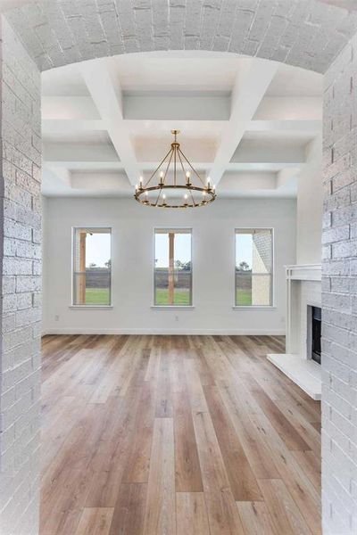 Unfurnished living room with light wood finished floors, coffered ceiling, beam ceiling, a fireplace, and a chandelier