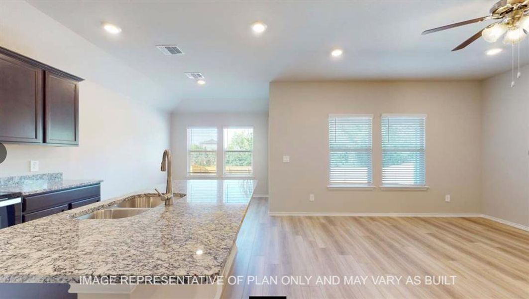 Kitchen with light stone countertops, dark wood finish cabinetry, light wood finished floors, a ceiling fan, and an island with sink