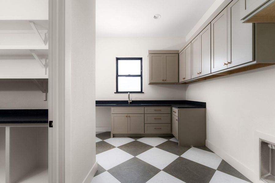 A well-appointed utility room features a functional sink, ample cabinetry, and striking checkerboard flooring.